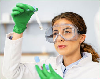A scientist in safety goggles examining a sample in a pipette tip